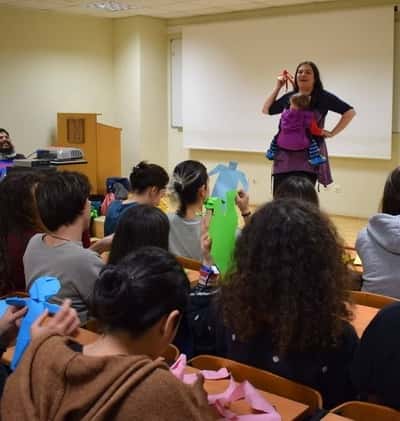 Η Αγγελική μιλάει σε μια τάξη παιδιά κρατώντας το παιδί της.